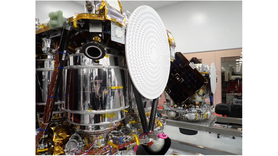 Two shiny silver spacecraft stand inside a large, clean room with white walls