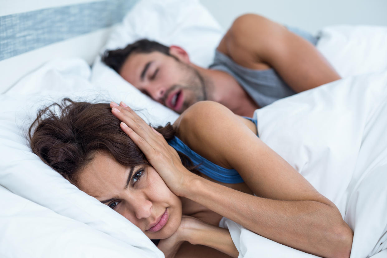 Portrait of woman blocking ears with hands while man snoring on bed