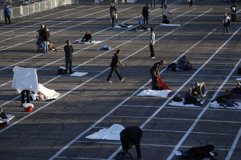 People prepare to sleep in areas marked by painted boxes on the ground of a parking lot at a makeshift camp for the homeless Monday, March 30, 2020, in Las Vegas. Officials opened part of the ot as a makeshift homeless shelter after a local shelter closed when a man staying there tested positive for the coronavirus. (AP Photo/John Locher)