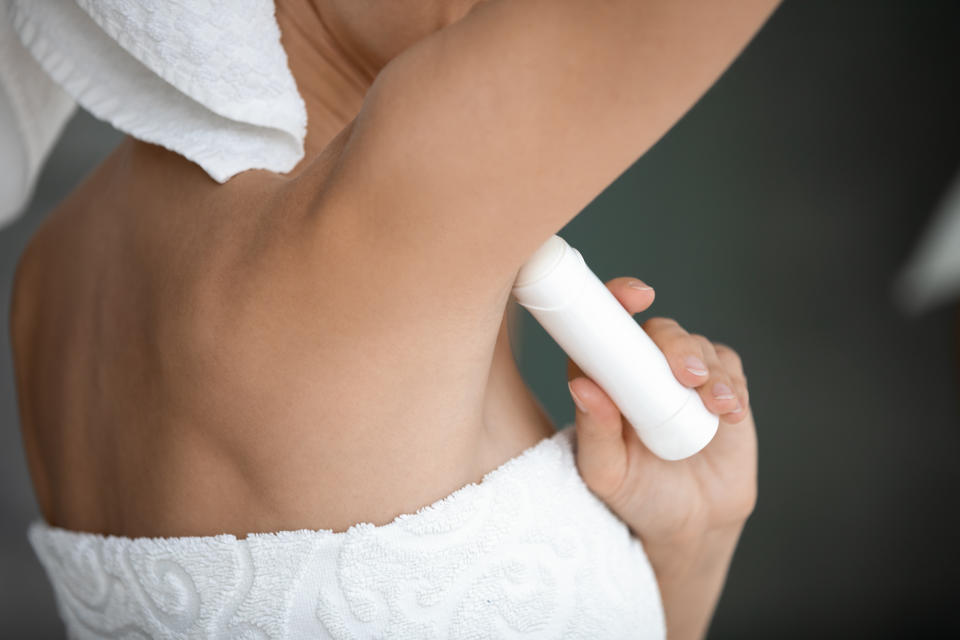 Young lady wrapped in white towel raise arm apply antiperspirant in armpit, woman use underarm deodorant stick for daily hygiene everyday freshness, hyperhidrosis treatment concept close up rear view