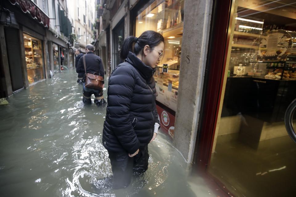 People wade their way through water in Venice, Italy, Friday, Nov. 15, 2019. Waters are rising in Venice where the tide is reaching exceptional levels just three days after the Italian lagoon city experienced its worst flooding in more than 50 years. (AP Photo/Luca Bruno)