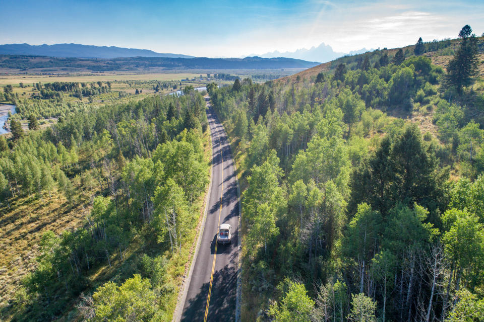 Aerial view of a winding road through a dense forest with mountains in the distance