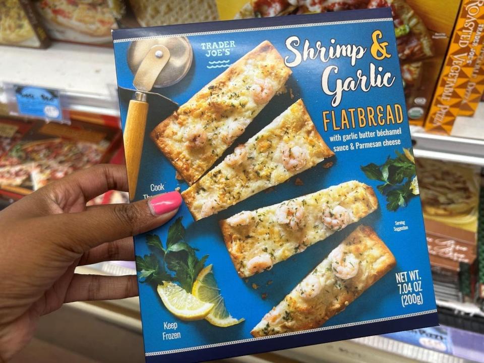 Woman holding a box of shrimp and garlic flatbread from Trader Joe's.