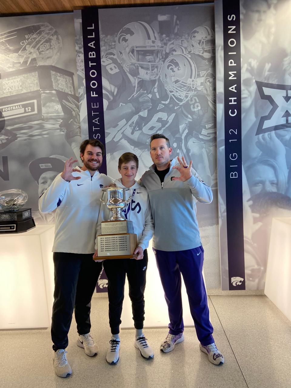 Kansas State football scouting analyst Chuck Lillie, from left, Hayden High School student Dylan Foster and Kansas State football director of football recruiting Taylor Braet hold the Governor's Cup during Foster's visit to Kansas State in March.