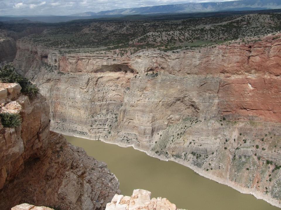 a brown river running through a deep, steep sided canyon with mountains in the background