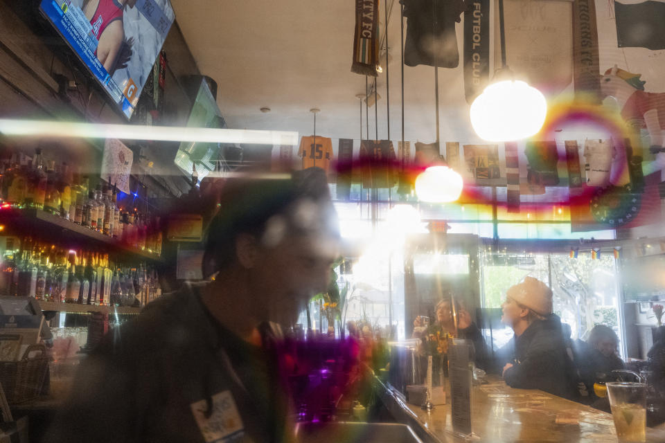 With a rainbow mustache drawn on a porthole door connecting the kitchen and bar, patrons watch a beach volleyball match on big-screen TV at The Sports Bra sports bar on Wednesday, April 24, 2024, in Portland, Ore. (AP Photo/Jenny Kane)