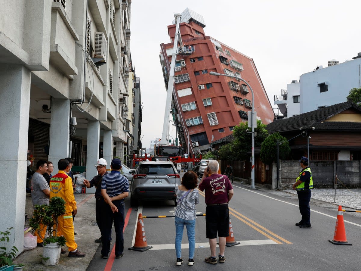 People look on as workers carry out operations on a partially-collapsed building following the earthquake (Reuters)