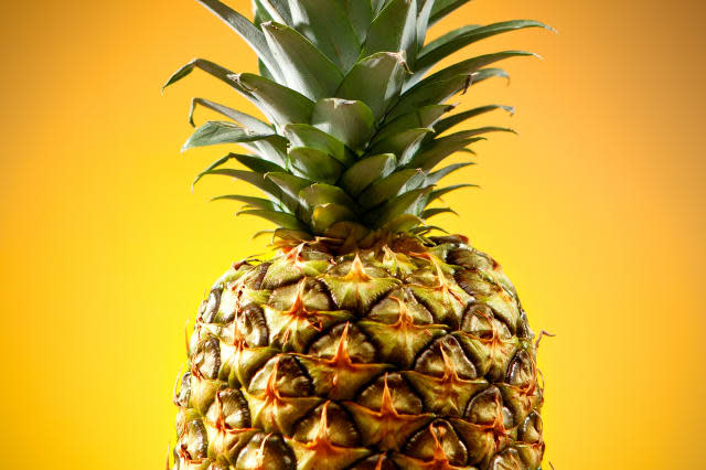 Pineapple with green leaves with bright yellow background.