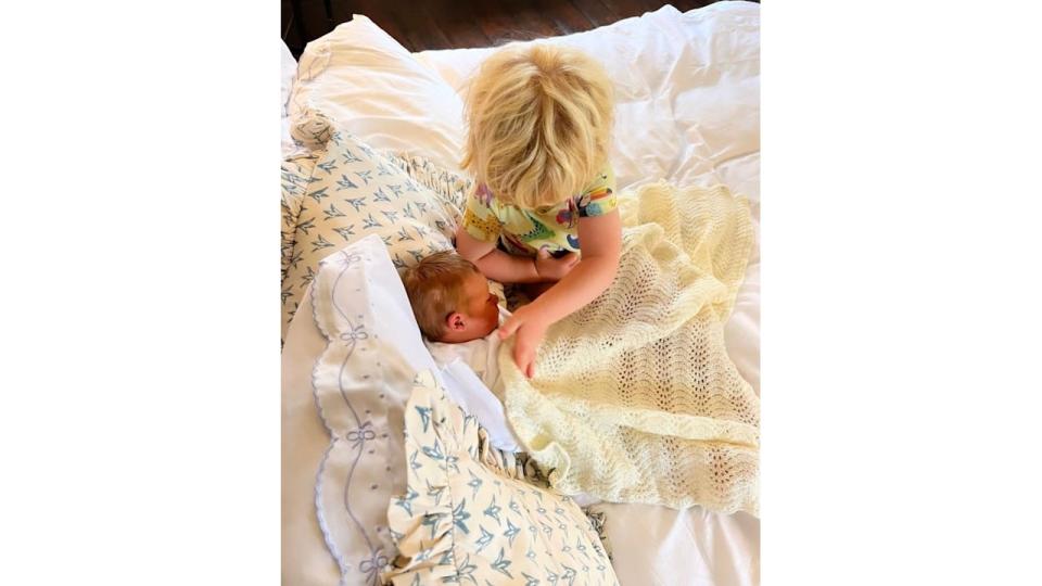 A blonde child putting a blanket over a baby