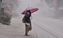 <p> A women walks on a road covered with volcanic ash following an eruption of Mount Kelud, in Yogyakarta, Indonesia, Friday, Feb 14, 2014. Volcanic ash from a major eruption in Indonesia shrouded a large swath of the country's most densely populated island on Friday, closed three international airports and sent thousands fleeing. (AP Photo/Slamet Riyadi) </p>