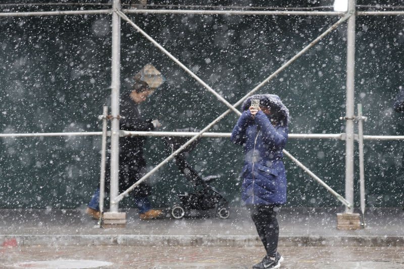 A pedestrian bundled up for cold freezing temperatures takes a photo of the New York Stock Exchange as snow falls accompanied by cold temperatures on Wall Street on Friday. Photo by John Angelillo/UPI