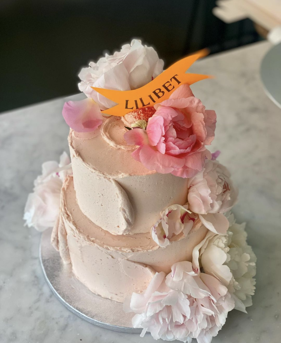 A tiered cake with pink buttercream icing and pink peonies. 