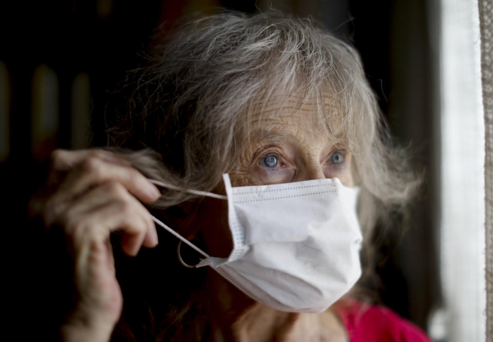 Carmela Corleto adjusts her mask as she peers out the window of her home where she lives alone and waits her turn to get a COVID-19 vaccine in Burzaco, Argentina, Thursday, Feb. 18, 2021. Corleto, who said she never imagined the lockdown would last so long, or that COVID-19 would be so contagious and dangerous, got her first shot of the AstraZeneca vaccine on April 23, 2021. (AP Photo/Natacha Pisarenko)