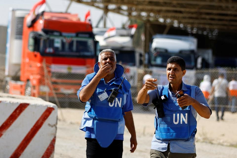 UN workers gesture as trucks carrying aid arrive at the Palestinian side of the border with Egypt, as the conflict between Israel and Palestinian Islamist group Hamas continues, in Rafah in the southern Gaza Strip, October 21, 2023.