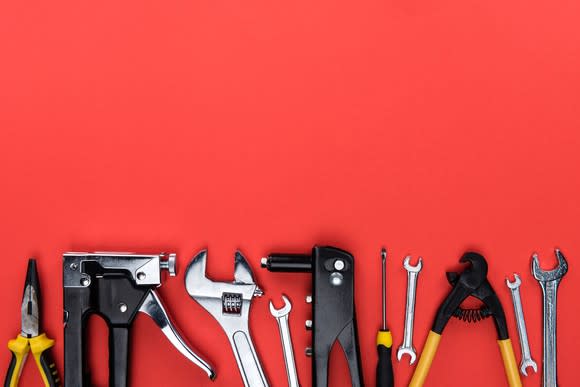 A set of workman's tools lined up against a red background.