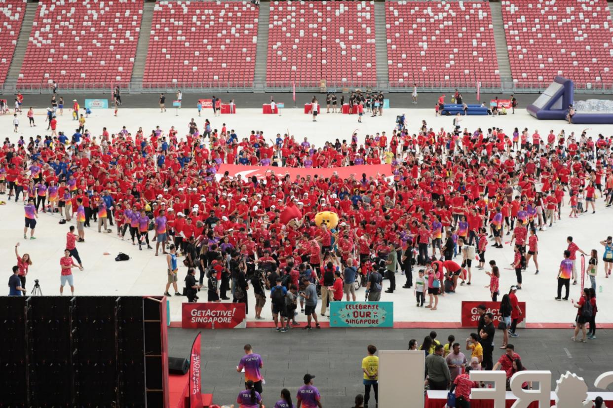 Volunteers and partners of the Get Active! Singapore sport fiesta form a heart formation with President Halimah Yacob and MCCY minister Grace Fu at the National Stadium (PHOTO: Sport Singapore)