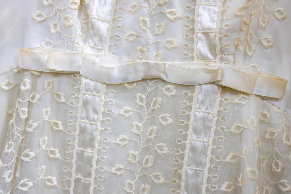 Close-up of a child's white dress with embroidered floral pattern and satin ribbon