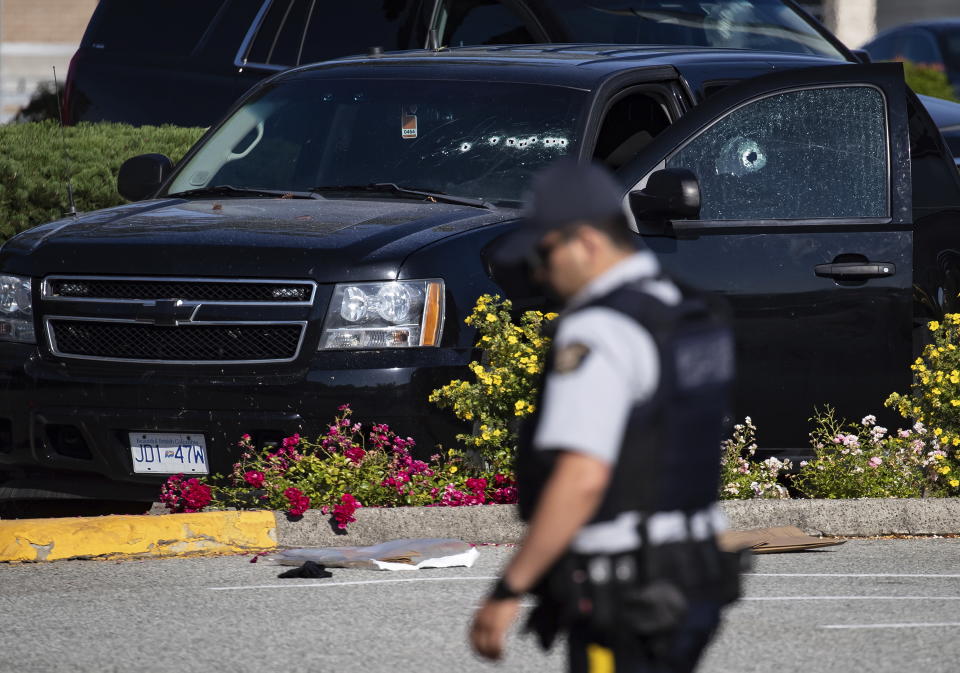 A police officer walks near a windshield and passenger window of an RCMP vehicle with bullet holes at the scene of a shooting in Langley, British Columbia, Monday, July 25, 2022. Canadian police reported multiple shootings of homeless people Monday in a Vancouver suburb and said a suspect was in custody. (Darryl Dyck/The Canadian Press via AP)