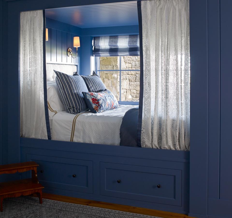 This guest room comes with a built-in queen-sized bed and its own custom privacy screen, which is covered in William Morris fabric. The Elkins sconces above the bed are by Thomas O’Brien and the custom rug is by Steven King Decorative Carpets in Boston. A mahogany step stool by Lostine Home Goods can be seen in the lower left corner. The room is painted Pitch Blue by Farrow & Ball.