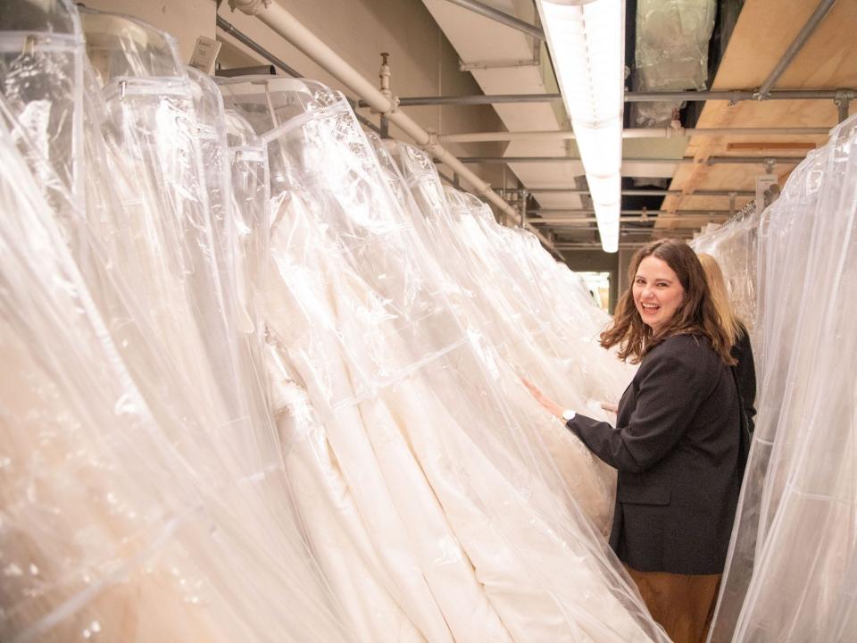 A woman smiles as she walks through a row of wedding dresses.