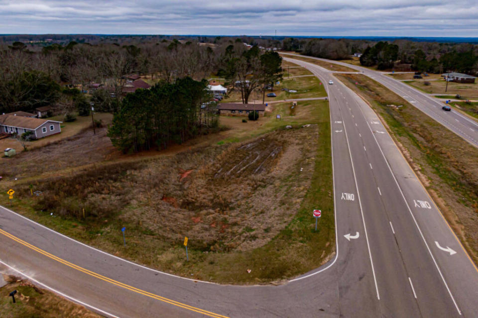 Roads stretching at an acute angle into the horizon, with trees, grass and a home between them