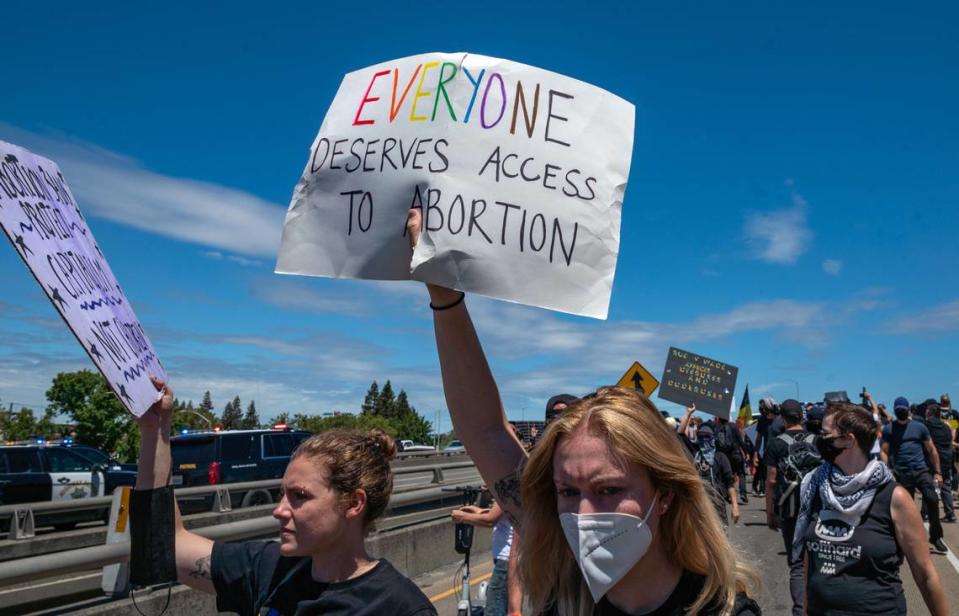 Abortion rights protesters hold signs on the northbound Interstate 5 on-ramp in downtown Sacramento on Monday, July 4, 2022, as police vehicles behind them mark the start of traffic stopped on the freeway.