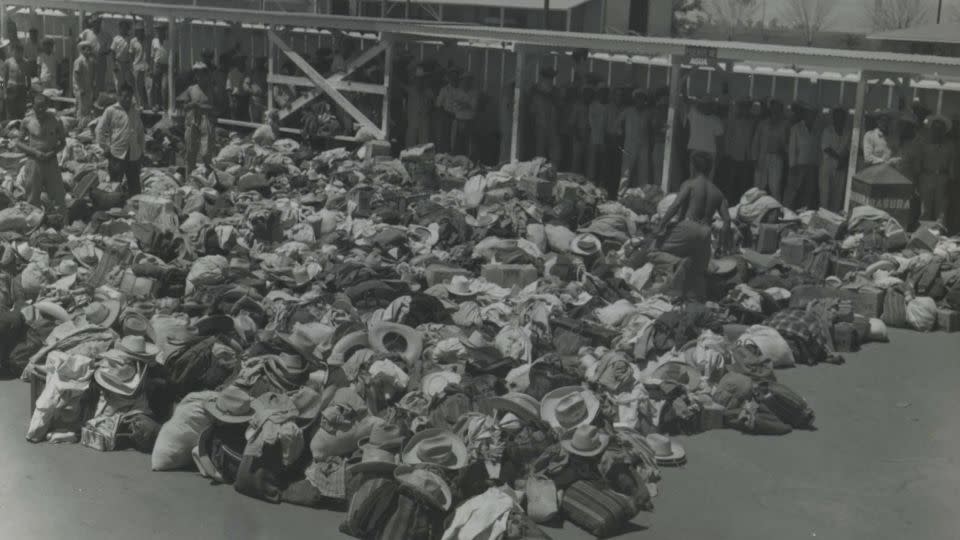 Aspiring <em>braceros</em> line up to undergo physical examinations by the US Public Health Service in South Texas in the 1950s. Their hats, bags and other belongings are piled nearby. - USCIS History Office and Library/Department of Homeland Security