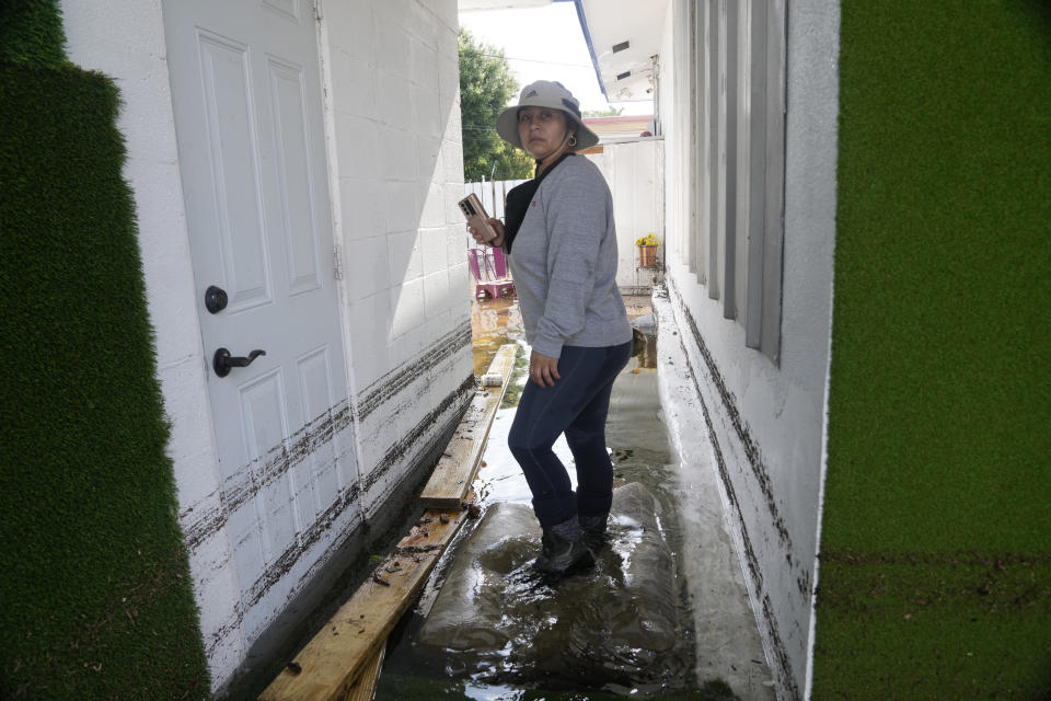 Claudia Rodriguez assess water damage to a neighbor's home, Friday, April 14, 2023, in Fort Lauderdale, Fla. South Florida has begun draining streets and otherwise cleaning up after an unprecedented storm that dumped upward of 2 feet of rain in a matter of hours. Gov. Ron DeSantis issues a state of emergency for Broward County, which sustained the worst flooding in decades. (AP Photo/Marta Lavandier)