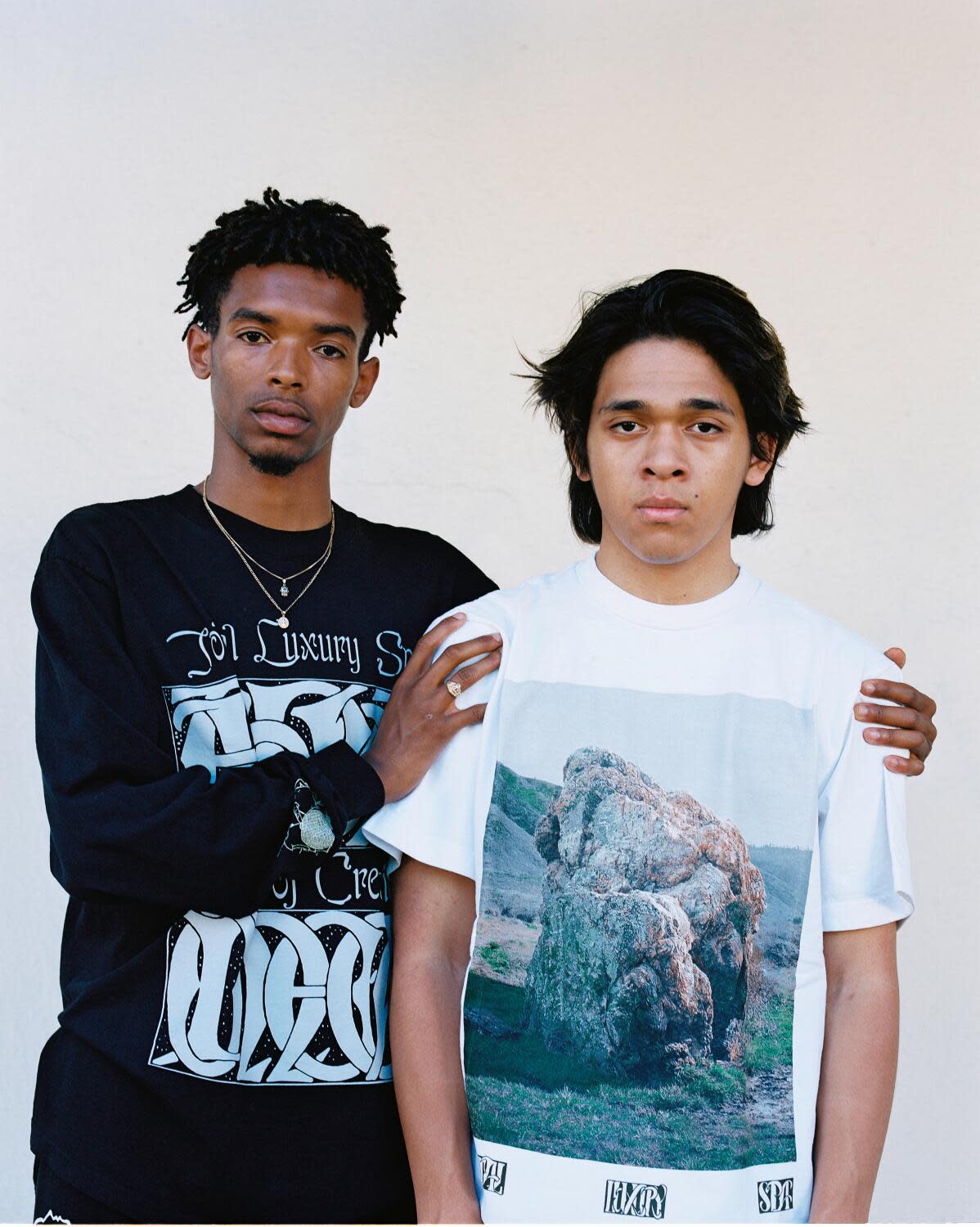 A young man in black T-shirt holds a young man in white T-shirt by the shoulders.