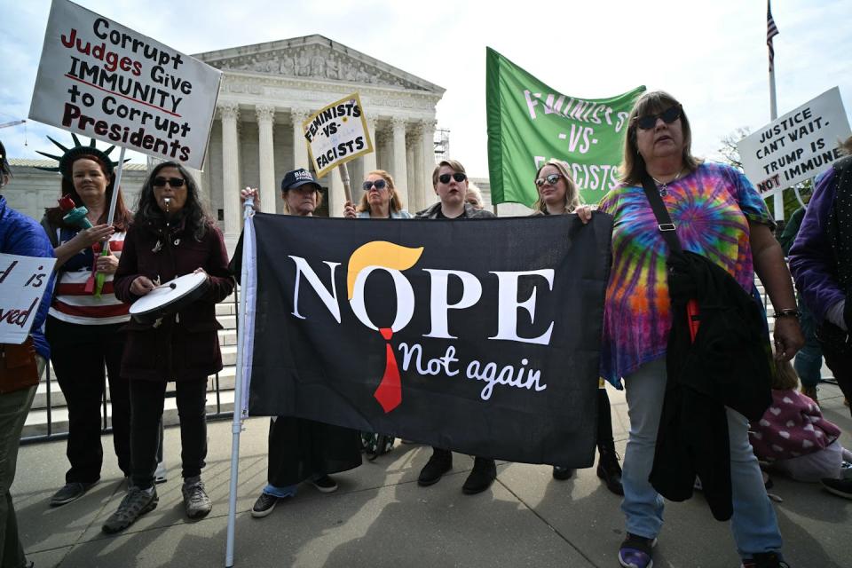 A group of people stand outside the Supreme Court and hold signs that say 'Corrupt judges give immunity to corrupt presidents' and 'Nope, not again.'