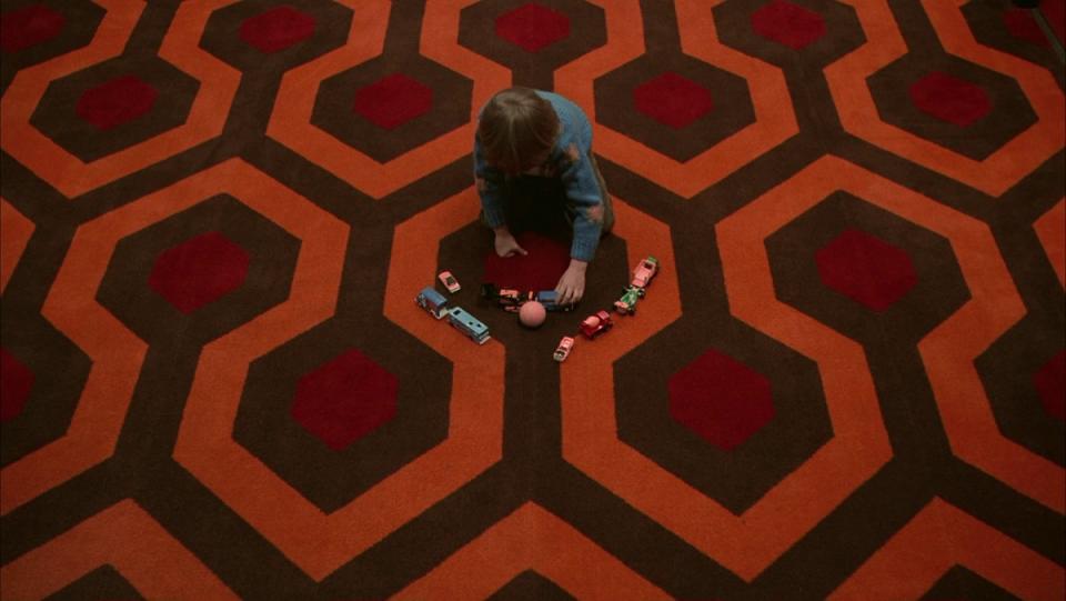 A young boy plays on a red brown and orange patterned carpet