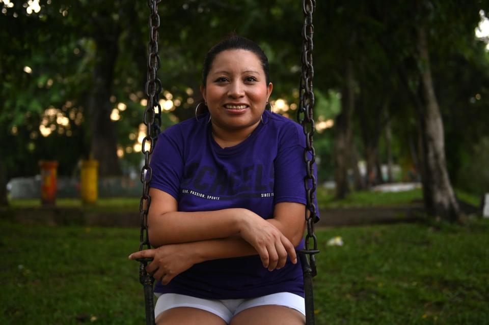 Woman in a purple T-shirt sits on a swing, smiling with arms crossed