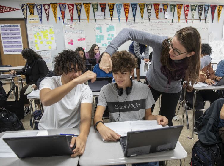 VAN NUYS, CA-NOVEMBER 17, 2022: William Lopez Rodas, left, sitting next to classmate Daniel Safa, both 10th graders at Birmingham High School in Van Nuys, receives a congratulatory fist bump from his teacher, Lindsay Humphrey, for referring to his notes during a computer science class offered by Stanford University. Birmingham High School and other L.A. schools are partnering with the National Education Equity Lab to offer Ivy League courses to underserved high school students. (Mel Melcon / Los Angeles Times)