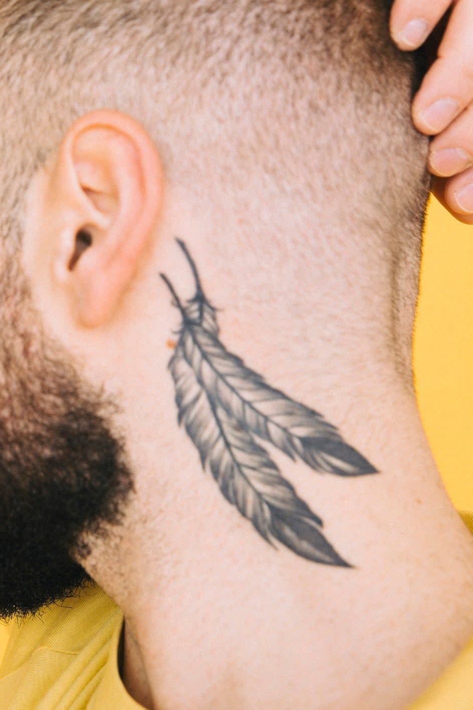 Man with a feather tattoo on the neck against a yellow background