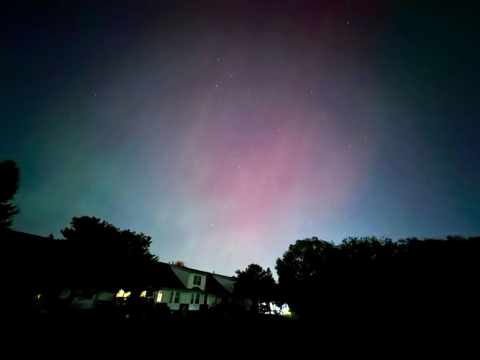 A night sky with aurora lights above a silhouette of houses and trees