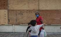 A family walks in front of a supermarket with its windows covered with plywood as Tropical Storm Zeta approaches Cancun, Mexico, Monday, Oct. 26, 2020. A strengthening Tropical Storm Zeta is expected to become a hurricane Monday as it heads toward the eastern end of Mexico's resort-dotted Yucatan Peninsula and then likely move on for a possible landfall on the central U.S. Gulf Coast at midweek. (AP Photo/Victor Ruiz Garcia)