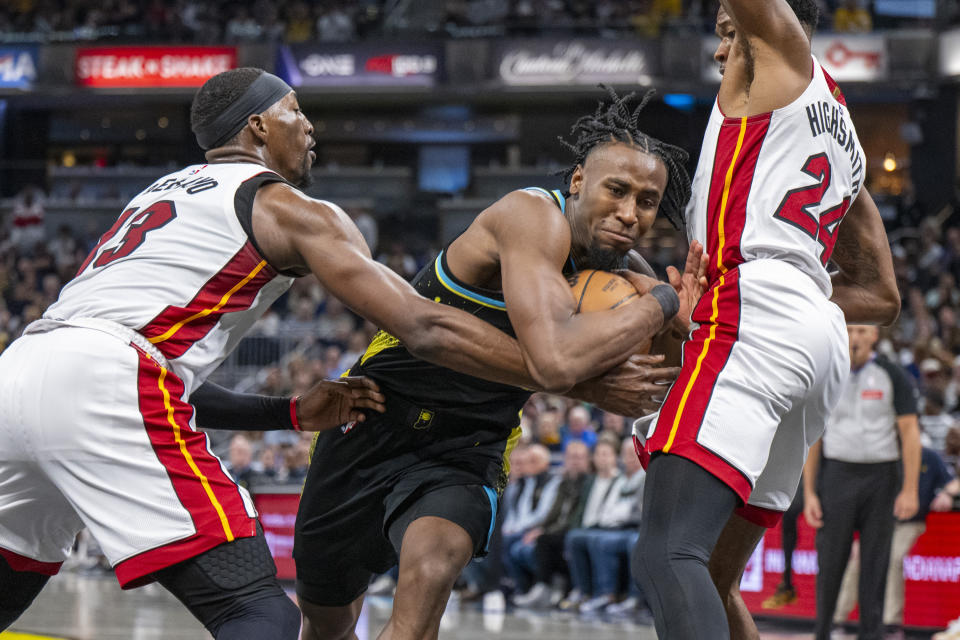 Indiana Pacers forward Aaron Nesmith, center, drives the ball into the defense of Miami Heat center Bam Adebayo, left, and forward Haywood Highsmith, right, during the second half of an NBA basketball game in Indianapolis, Sunday, April 7, 2024. (AP Photo/Doug McSchooler)