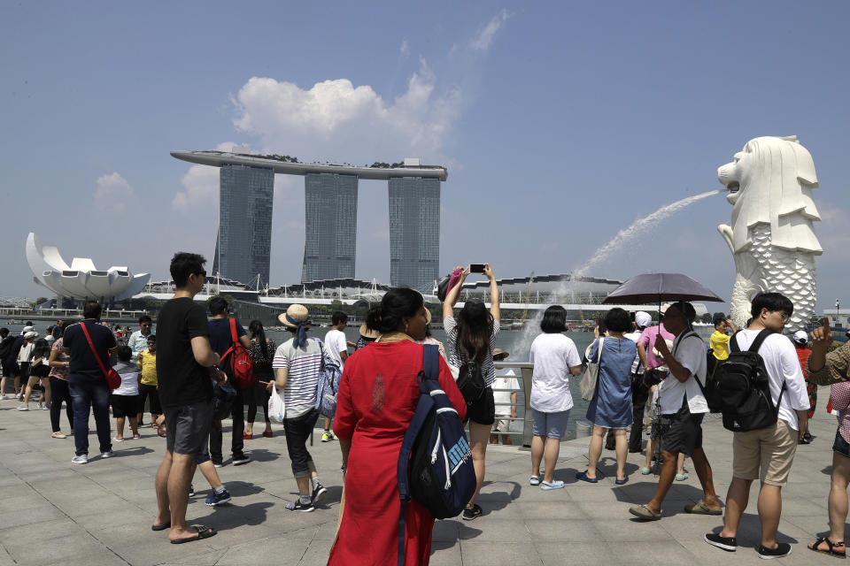 FILE - In this June 7, 2018, file photo, tourists photograph the Merlion, right, one of the icons of Singapore, with the Marina Bay Sands in the background. On Wednesday, April 3, 2019, casino company Las Vegas Sands announced it'll spend $3.3 billion to expand its property in Singapore by adding an entertainment arena, another hotel tower and additional convention space. (AP Photo/Wong Maye-E, File)