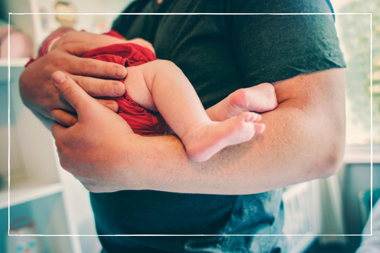  Close up of a man in dark t shirt holding a newborn baby in his arms 