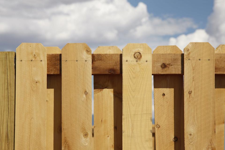 A light-colored wooden fence against a cloudy sky.