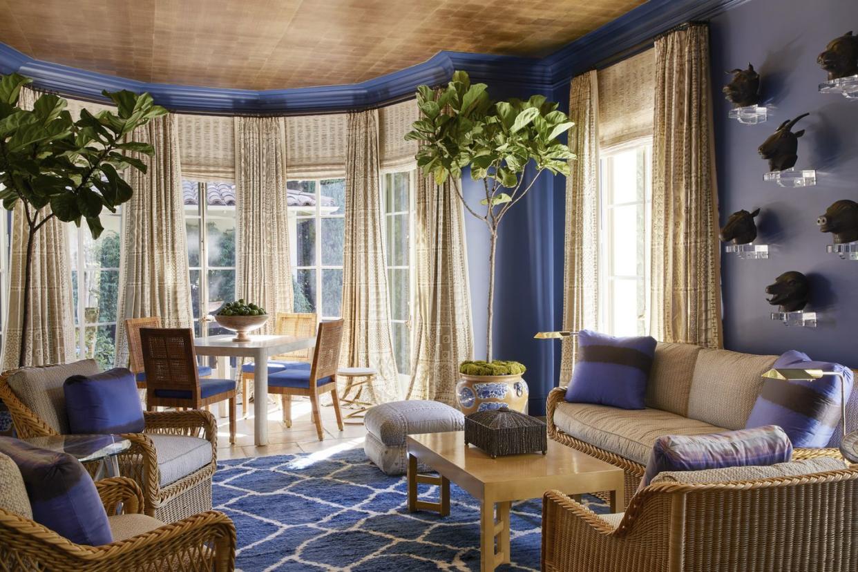 fortuny barkcloth and cotton fabrics cover wicker seating and windows respectively in the deep blue sunroom