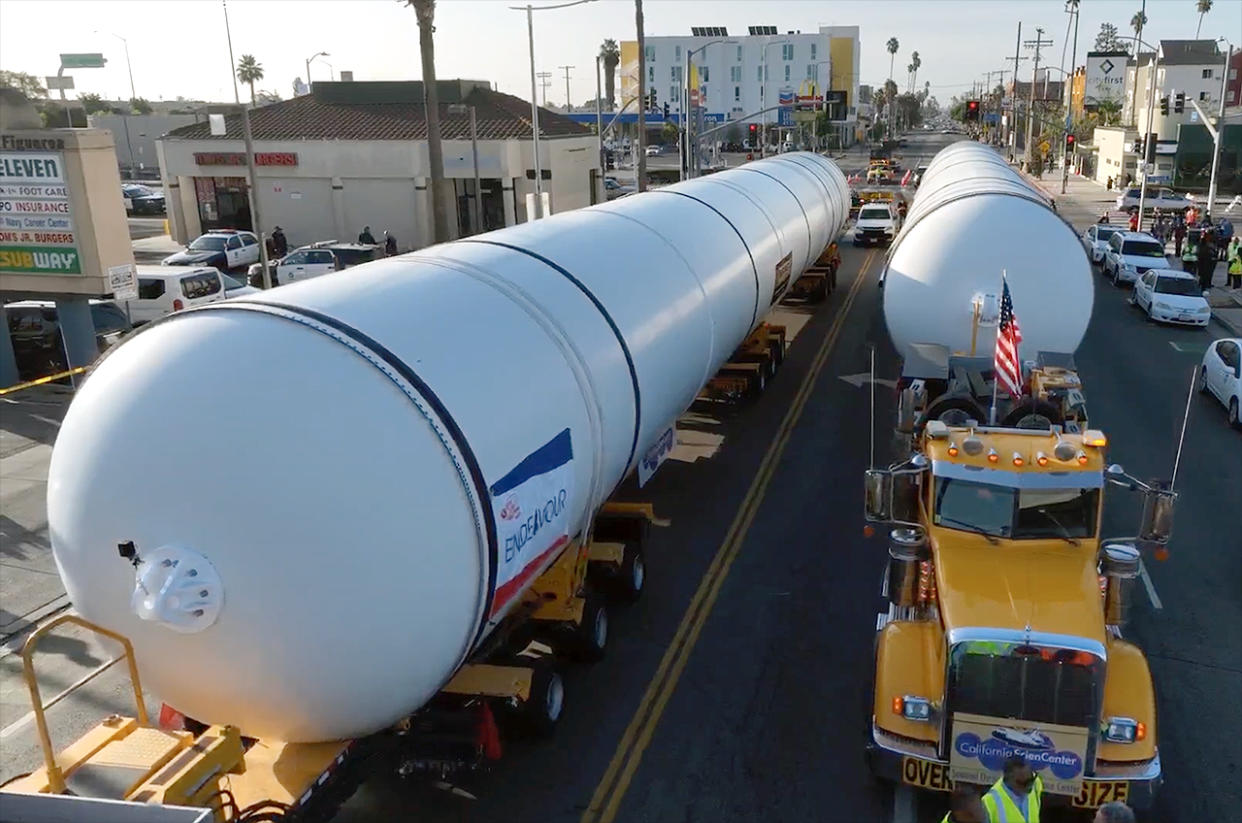  Trucks tow two big white cylindrical rocket motors through the streets of los angeles. 