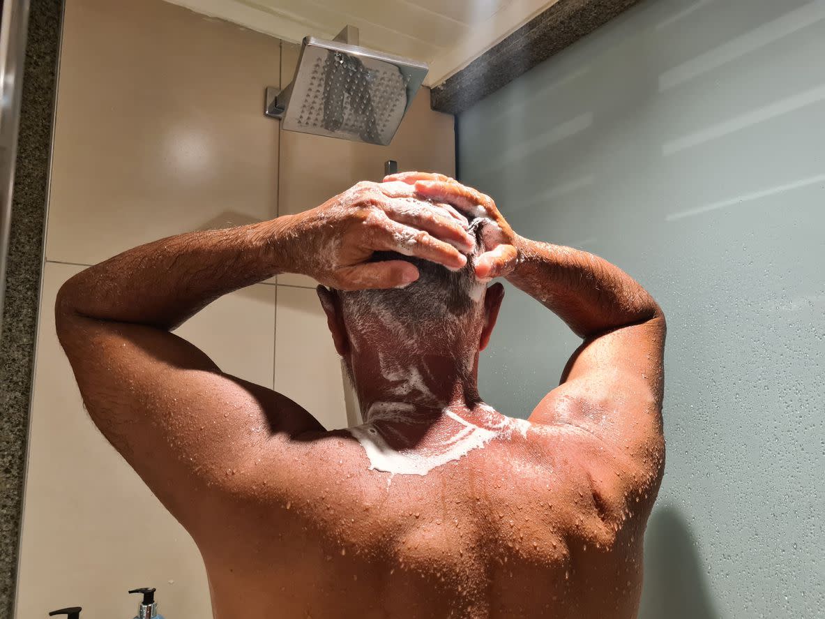 Older man washes hair and uses shampoo in shower