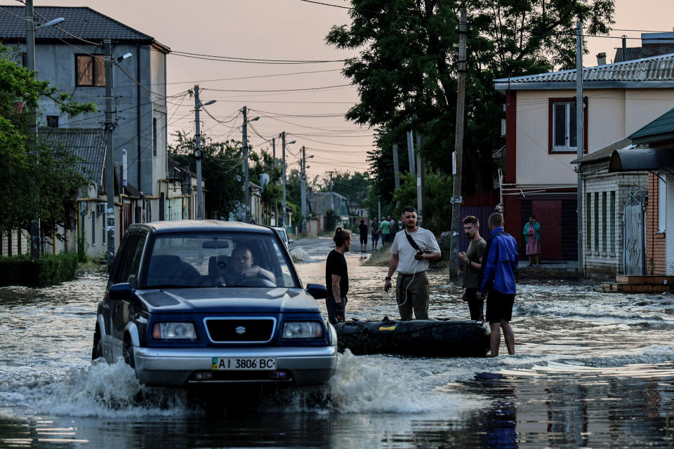 A car makes its way past people standing next to an inflatable boat, in a flooded street of Kherson on June 6.<span class="copyright">Ivan Antypenko—EPA-EFE/Shutterstock</span>
