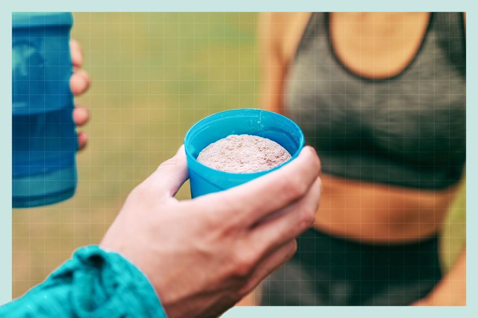 A hand holding a container full of protein powder ready to go into a protein shake. in the background is a shake bottle and a woman in workout clothes