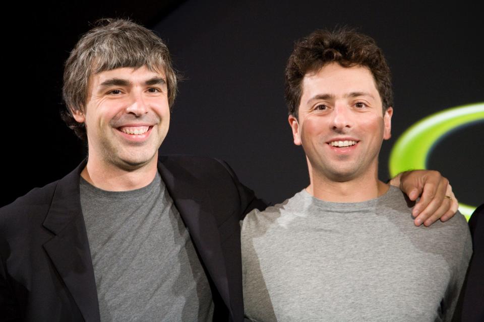 Google cofounders Larry Page and Sergey Brin stand with their arms around one another.