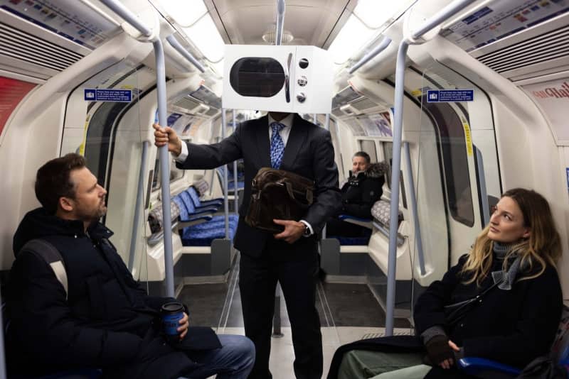 A man on the underground in London with a microwave on his head protesting against ultra processed convenience foods leading to a health crisis. David Parry/PA Wire/dpa