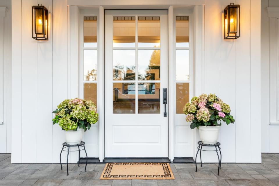 front porch with lanterns, flowers on each side of the door and brown doormat