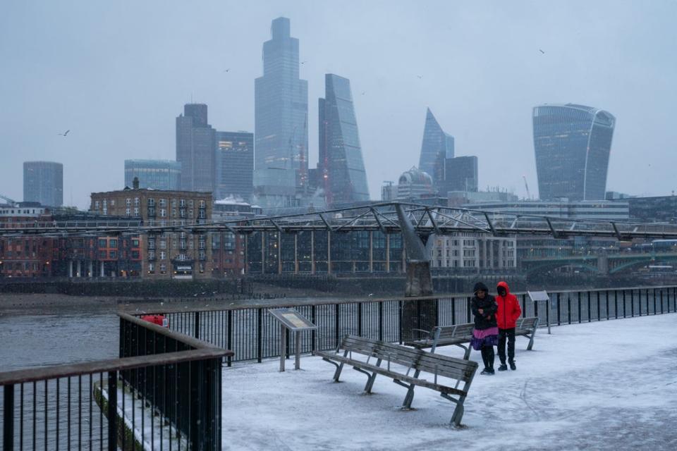 People walk on the south bank of the river Thames in London during a snow shower in February (PA)