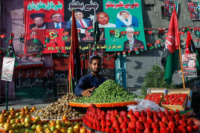 Fruit vendor waits for customers in front of a makeshift office with campaign posters of a political party, ahead of general elections, in Karachi